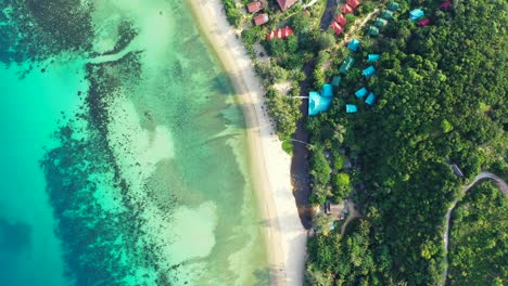 Peaceful-white-sandy-beach-washed-by-colorful-pattern-of-calm-lagoon-with-coral-reefs-and-pebbles-seabed-in-front-of-holiday-resort