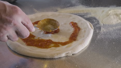 close up view of a chef spreading sauce on pizza dough on a restaurant kitchen countertop