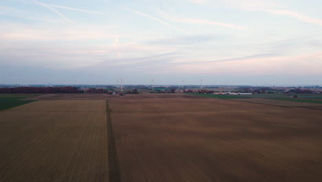 Ackerland-Mit-Sauberen-Reihen-Und-Linien,-Während-Wolkenschatten-Darüber-Ziehen,-Windkraftanlagen-In-Der-Ferne