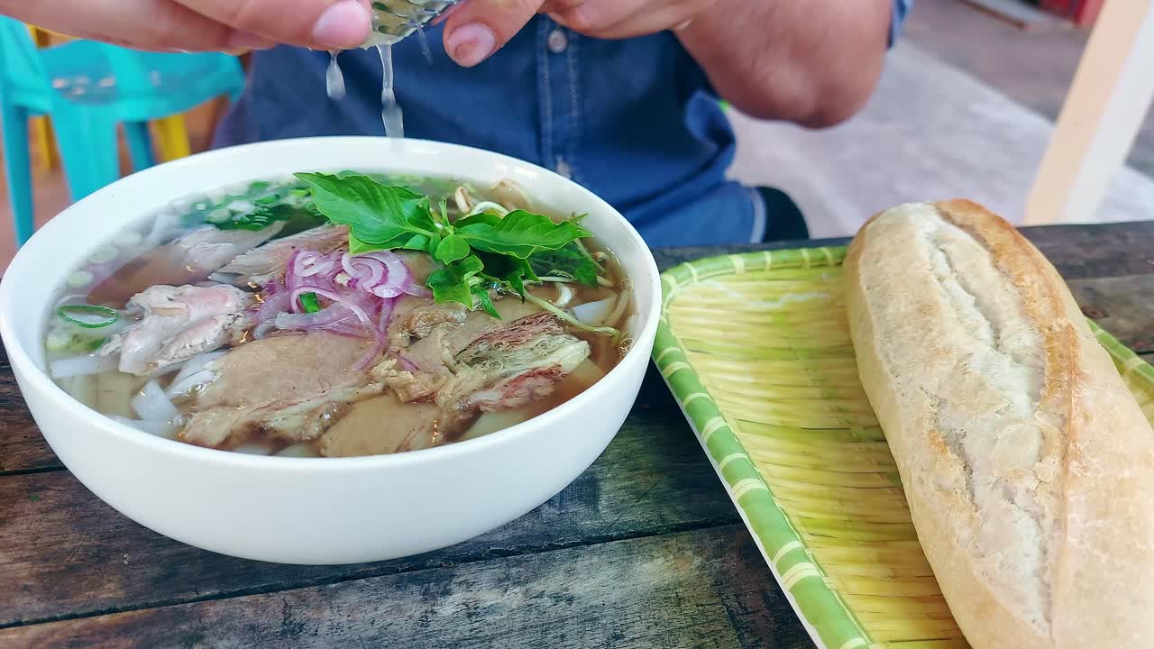 Squeezing lime over a bowl of pho bo or traditional Vietnamese beef noodle soup, authentic local food from Vietnam