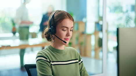 una mujer con auriculares y sonriendo en su escritorio en una oficina.