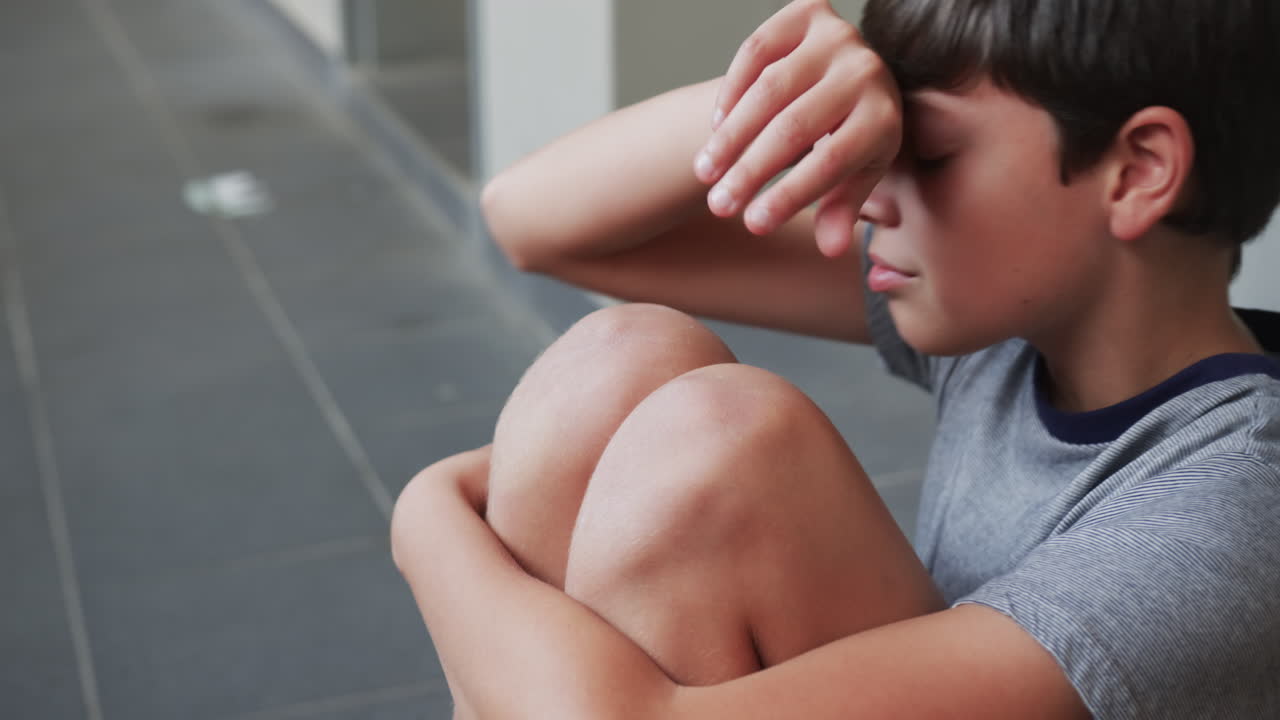 Crying boy sitting on floor in school hallway, feeling sad and upset