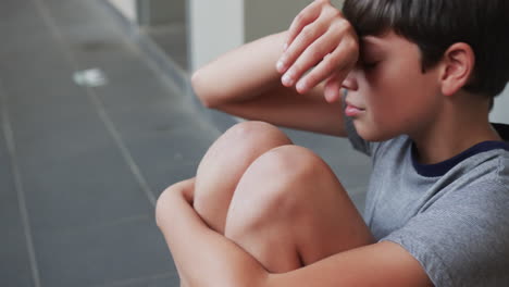 crying boy sitting on floor in school hallway, feeling sad and upset