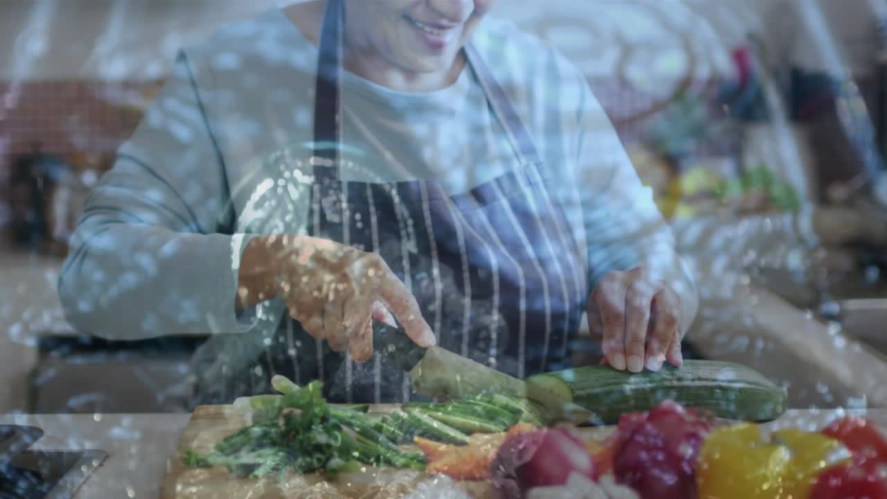 Senior woman placing cucumber on board, slicing with chef's knife for cooking amid water bubbles
