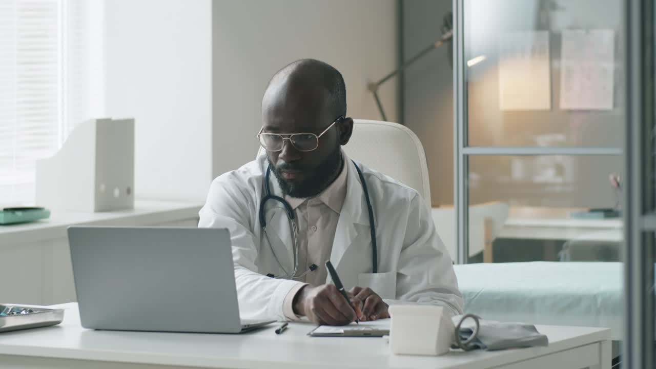 Black Doctor Working on Laptop and Taking Notes