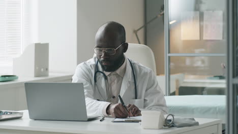 black doctor working on laptop and taking notes