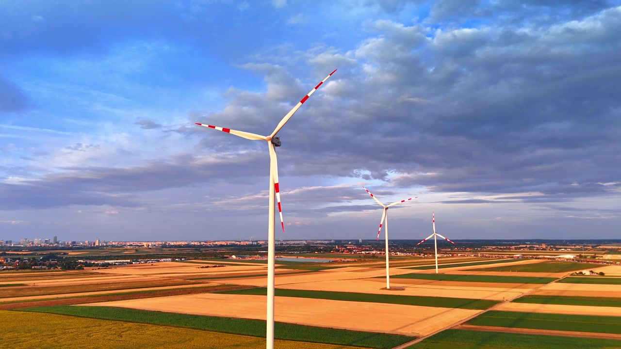 Turbine eoliche in funzione nei campi agricoli sotto un cielo nuvoloso. Vista dall'alto di strutture per l'energia alternativa circondate da colture gialle con l'orizzonte della città sotto scure nuvole di pioggia.