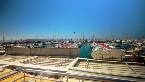 a busy marina filled with docked boats and yachts under a clear blue sky, with a view of the sea and port facilities