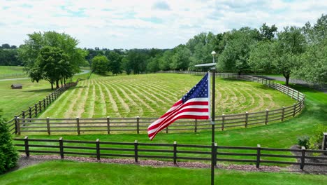 american flag waving in front of fenced in meadow for horses in usa