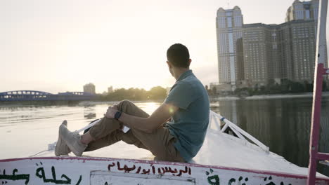 Pulling-away-revealing-man-sitting-on-bow-of-boat-watching-sunrise,-slow-motion