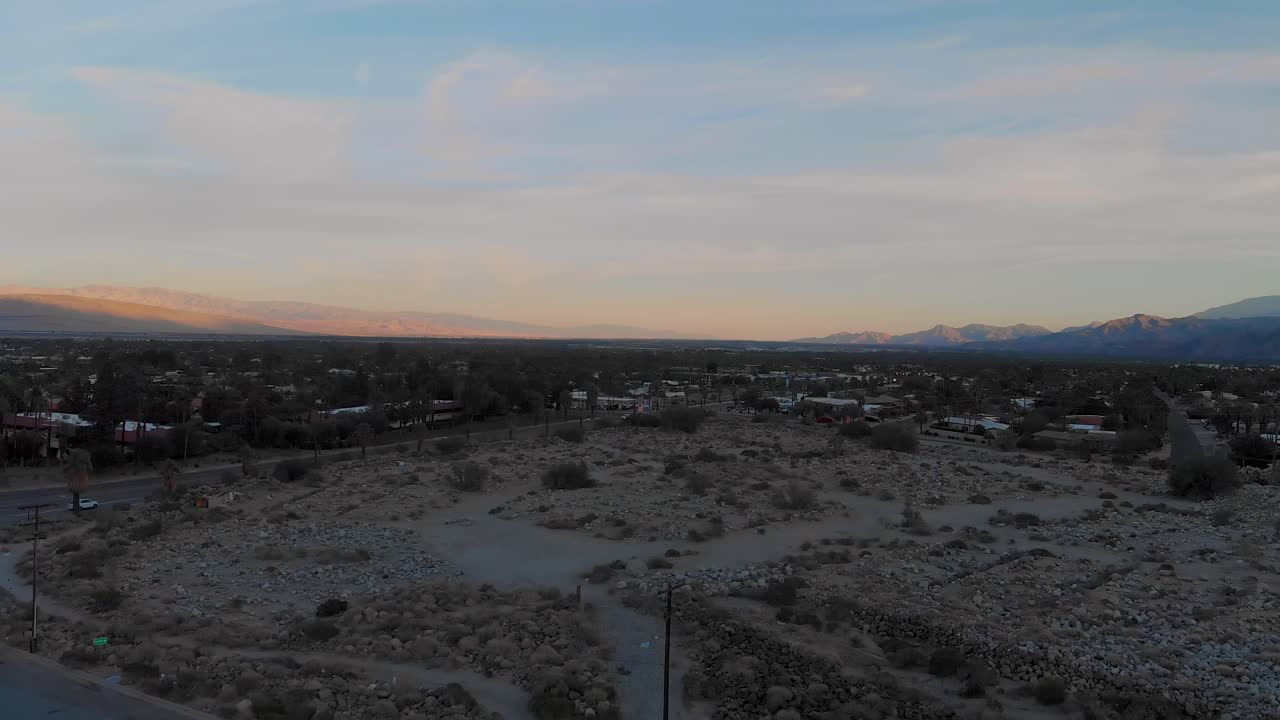 Drone che si alza sopra colline coperte di sabbia e arbusti fuori da una piccola città desertica