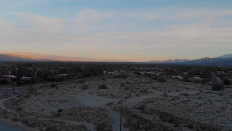 Drone-fly-up-over-of-sand-and-brush-covered-hills-outside-small-desert-town