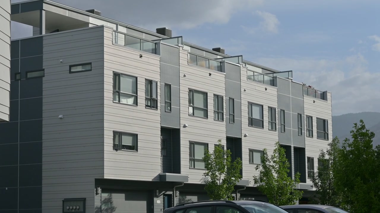 ブリティッシュコロンビア州ペンティクトンにて、一部曇り空の下、バルコニーと手前の木々が特徴的な現代的な集合住宅の静止画
