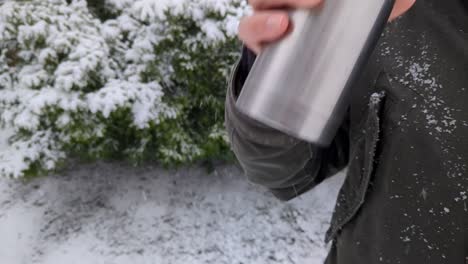 beber bebida caliente de un termo mientras nieva en un día de invierno al aire libre, cerca