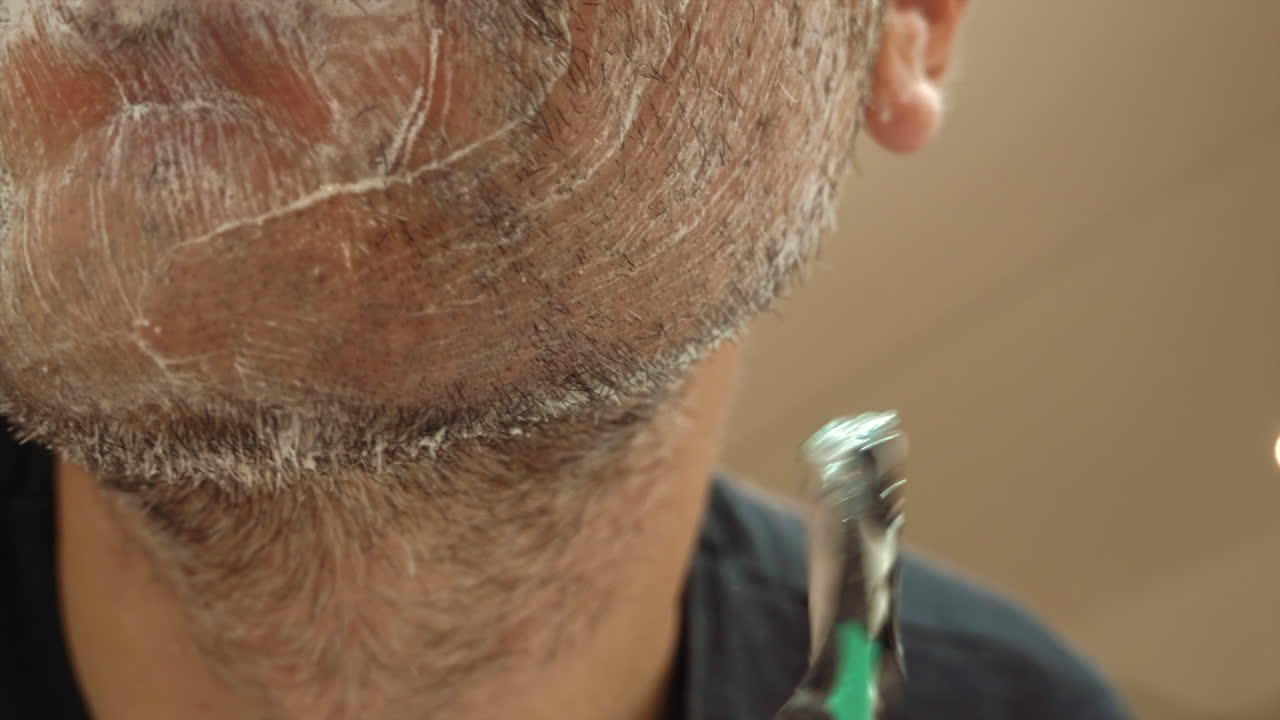 Close up of a man shaving his beard with a green and black razor