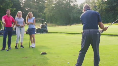 parejas maduras y medias adultas jugando una ronda de golf juntas viendo a un hombre hacer un tiro de tee