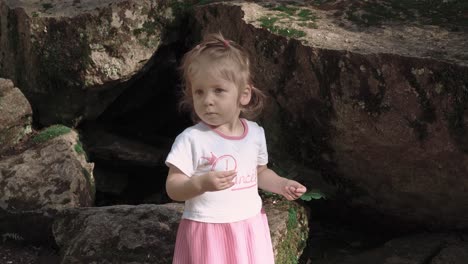 Portrait-of-a-little-girl-near-big-stones-in-the-forest-which-looks-for-something-close-up