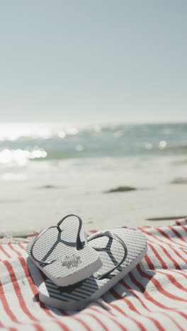 vertical video of flip flops and towel on beach, in slow motion, with copy space