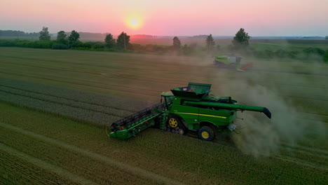 Luftdrohnenaufnahme-über-Einem-Grünen-Mähdrescher,-Der-Auf-Einem-Reifen-Maisfeld-Erntet,-Während-Sich-An-Einem-Herbstabend-Ein-Anderer-Mähdrescher-Im-Hintergrund-Bewegt