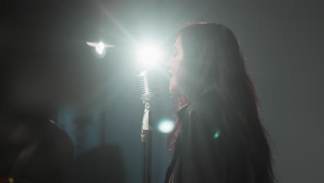 a singer in a black leather jacket sings with emotion, moving her hands expressively. bright light shines on her face, creating a dramatic effect in the background