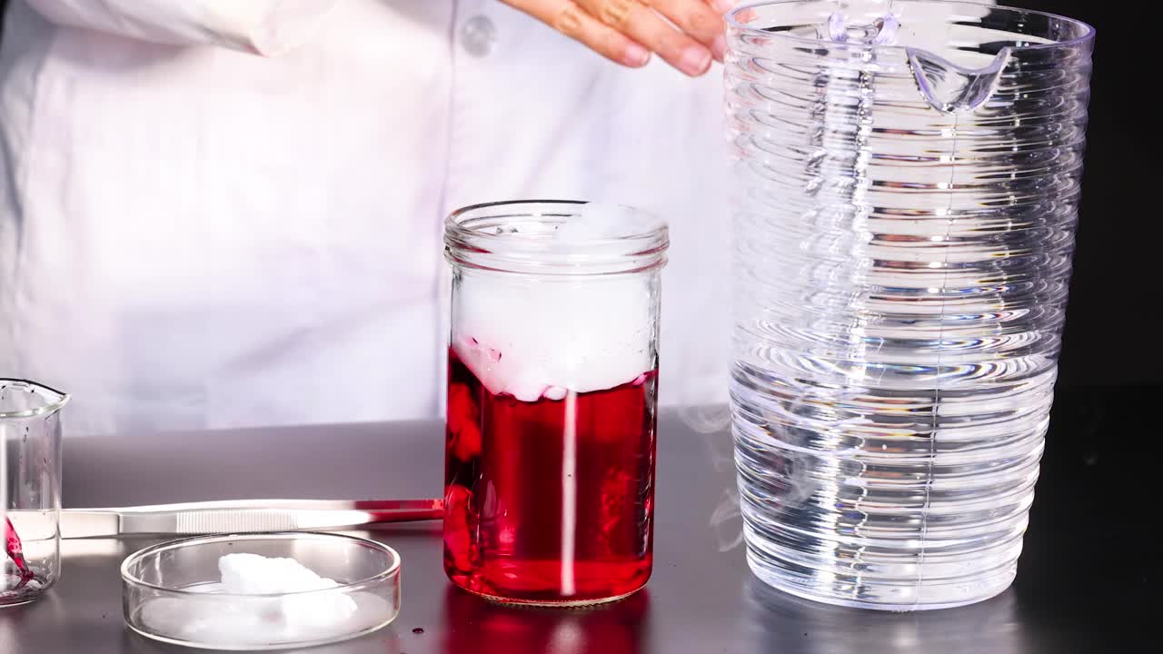 과학자가 실험실 환경에서 건조한 얼음과 색의 액체를 사용하여 연기 효과를 만드는 화학 반응을 시연합니다.