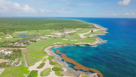 aerial wide shot of turquoise coastline o caribbean sea beside golf court in punta cana