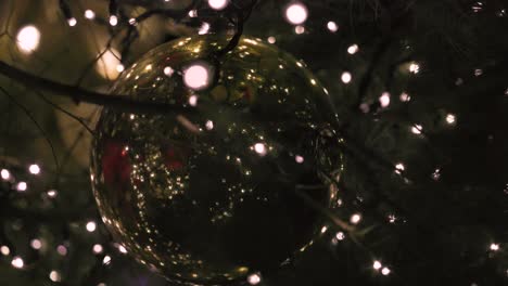 Giant-Golden-Christmas-Ornament-Ball-inside-big-Christmas-tree-with-Blinking-out-of-focus-Bokeh-Light-bulb