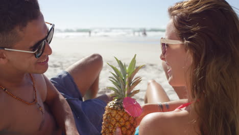 una pareja multirracial bebiendo cócteles de piña en la playa.