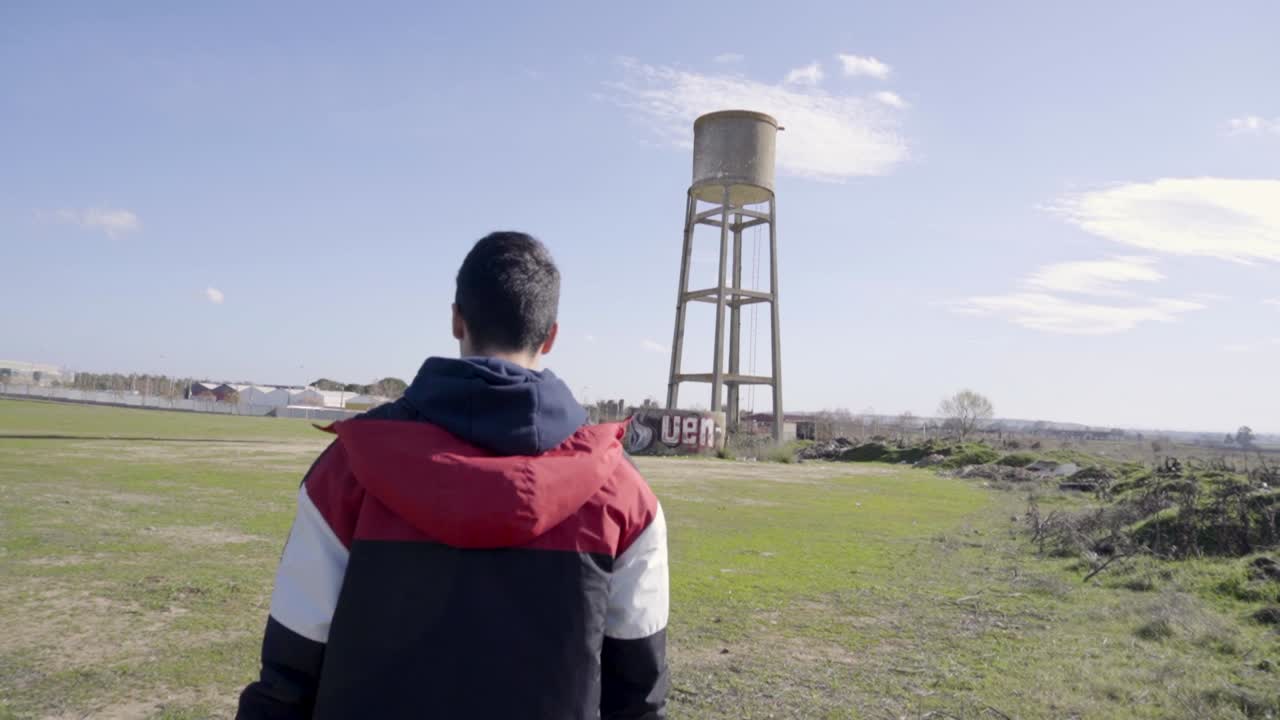Ragazzo che cammina verso una torre dell'acqua in un campo