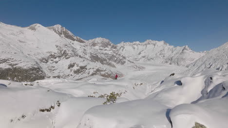 toma aérea en suiza con una persona caminando con raquetas de nieve en un día soleado con un glaciar detrás
