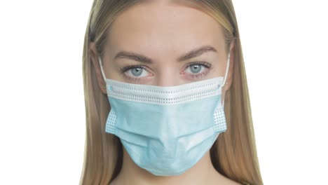 a young blonde woman wearing a surgical mask turns to look at the camera