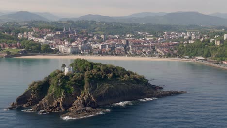 casa solitaria en una pequeña isla rocosa con la ciudad de san sebastián al fondo, vista aérea cinematográfica