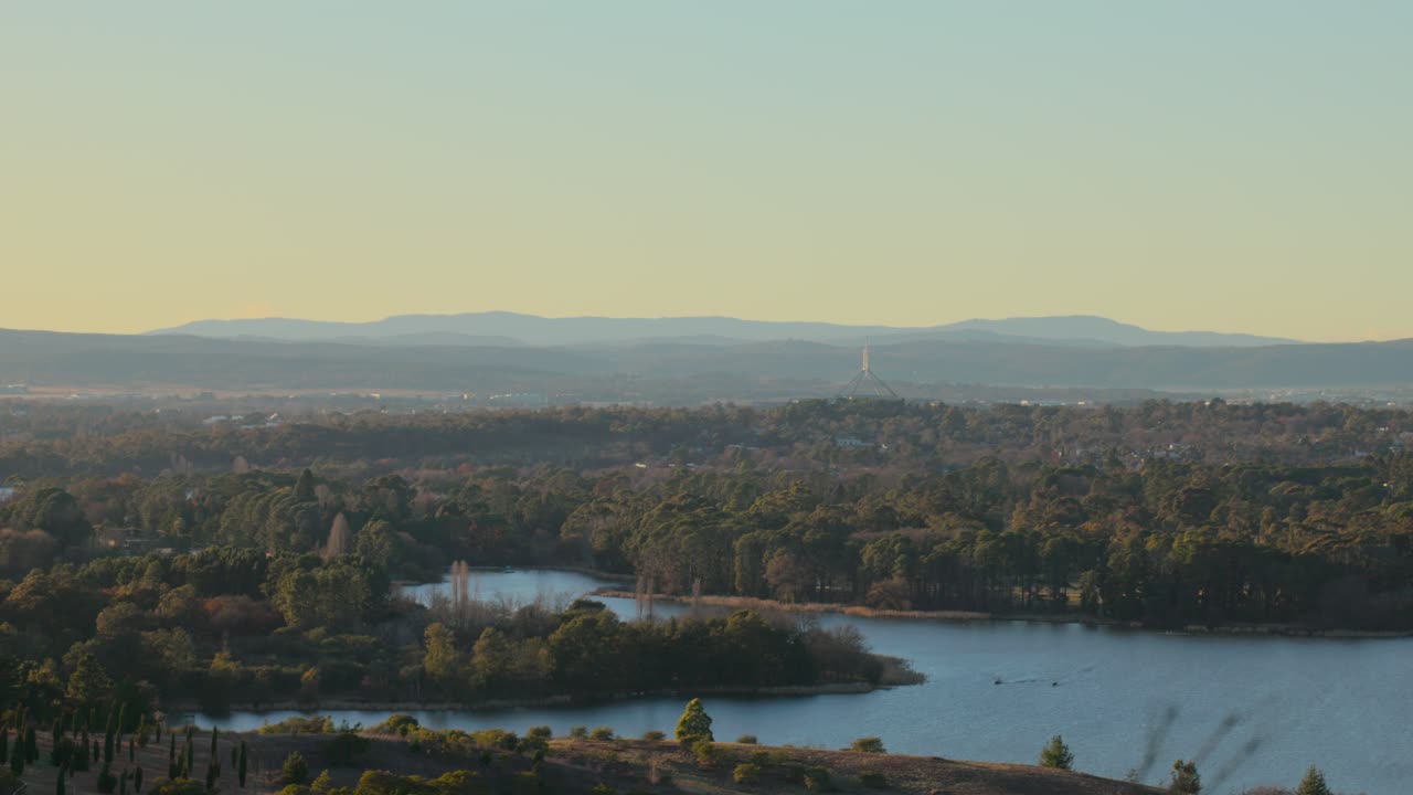 Elevated view of Canberra at sunrise with the Parliament House spire and tree-covered suburbs stretching toward the horizon