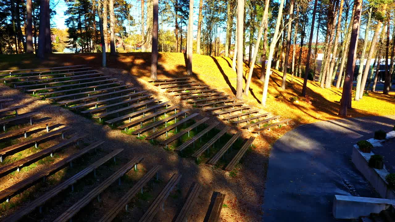 Open-air stage structure with wooden seating surrounded by trees in golden autumn light
