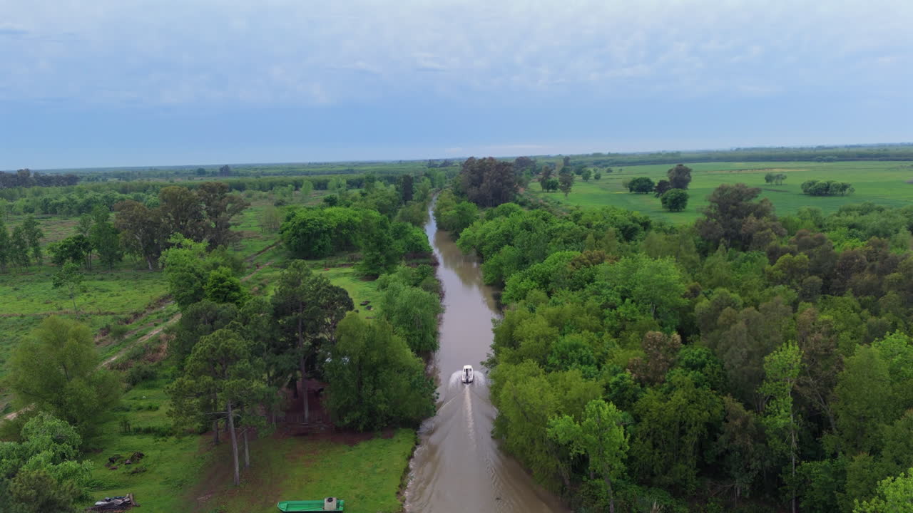 Rising aerial of small boat on calm muddy river in green Argentina landscape
