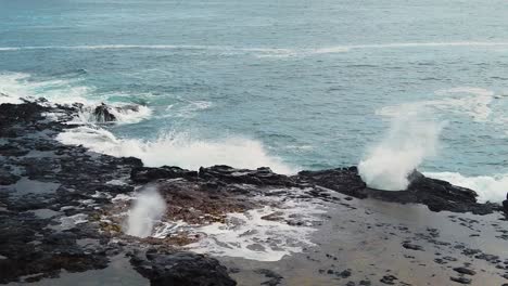 hd hawaii kauai pan left from spouting horn going off in left center frame to water swirling in hole in lava rock in left of frame with blowhole going off in right of frame with ocean in distance