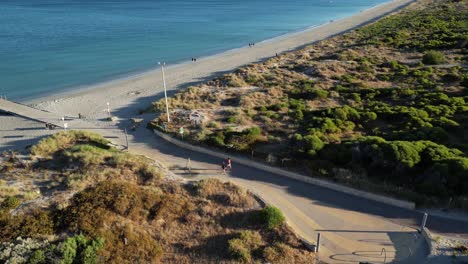 Toma-Aérea-De-Una-Pareja-Que-Llega-A-La-Playa-De-Woodman-Point-En-La-Ciudad-De-Perth-Durante-Un-Hermoso-Día-Soleado---Colinas-De-Dunas-Verdes,-Playa-De-Arena-Y-Océano-Azul---Cámara-Lenta