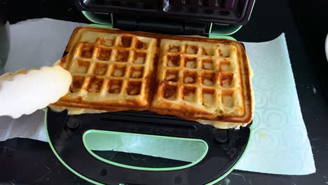 removing hot waffles from the waffle maker with plastic tongs - close up slow motion