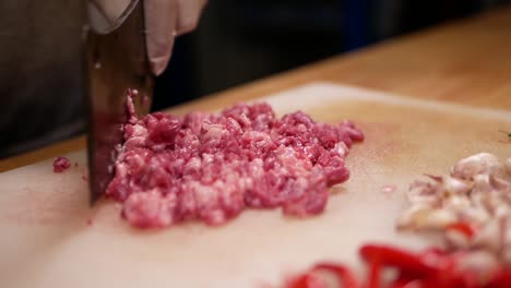 hand with glove chopping raw beef with pad kra paw ingredient on white chopping board, close up-1