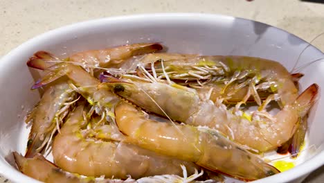 hand sprinkles salt on prawns in a dish