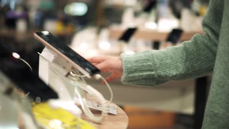 Unrecognizable-woman-chooses-a-new-smartphone-in-an-electronics-store