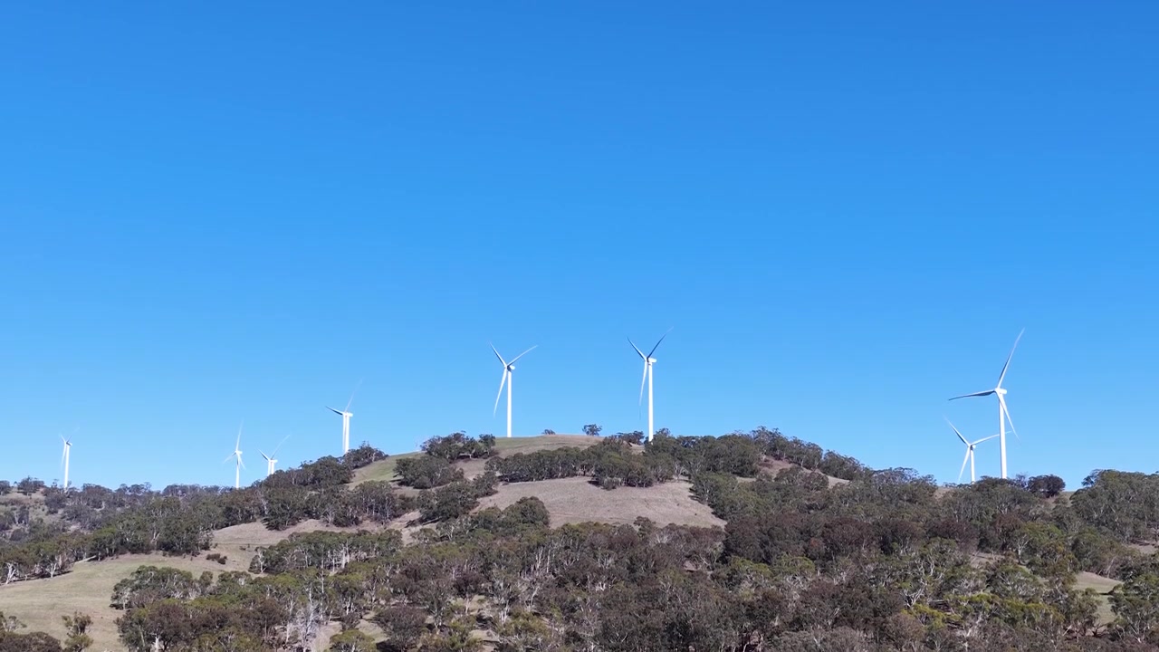 Ampia inquadratura di turbine eoliche per energia rinnovabile che girano su una collina rurale australiana sotto la luce del sole