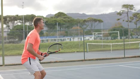 Two-diverse-male-friends-playing-doubles-returning-ball-on-outdoor-tennis-court-in-slow-motion