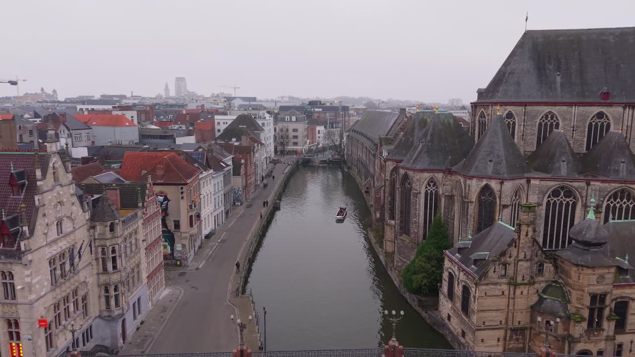 Il drone si allontana da una barca turistica vicino alla Chiesa di San Michele, rivelando il ponte iconico e lo splendido paesaggio urbano medievale di Gand lungo il fiume Leie
