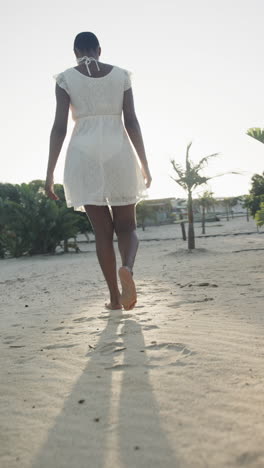 vertical video of african american woman in sundress walking barefoot on beach, slow motion