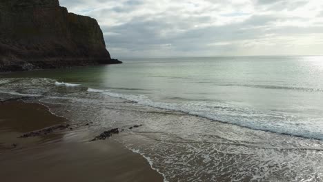 Sea-Waves-Gently-Rolling-into-Mewslade-Bay-with-Coastal-Cliffs-and-Dramatic-Cloudy-Sky-and-Sandy-Beach---Aerial-Drone-Shot-4K