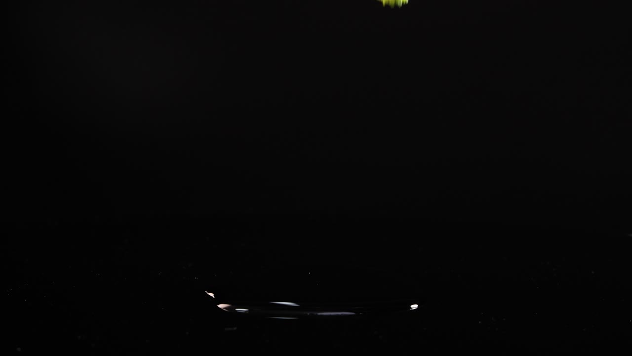 Broccoli florets fall onto a reflective black surface, captured in slow motion with dramatic lighting