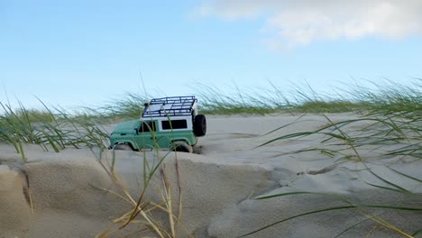 pequeña unidad de juguete de coche jeep de control remoto en dunas de arena con plantas costeras, vista estática
