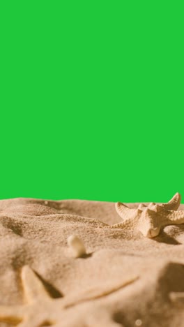 Vertical-Video-Summer-Holiday-Concept-With-Shells-Starfish-On-Sandy-Beach-Against-Green-Screen