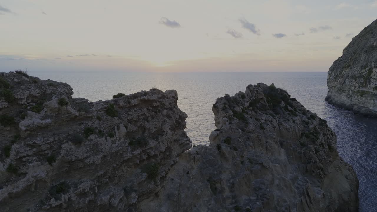 A calm drone approach through Xaqqa Valley heads toward the rugged cliffs, with warm sunset light and the open sea visible in the background